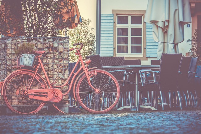 Ein rotes Fahrrad steht in der Sonne auf dem Gehweg vor einem Cafe.